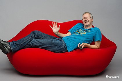 Manfred Scheucher sitzt auf einem roten 70er Jahre Sofa